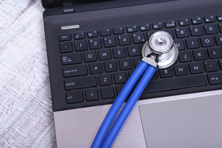 A medical stethoscope near a laptop on a wooden table, on white