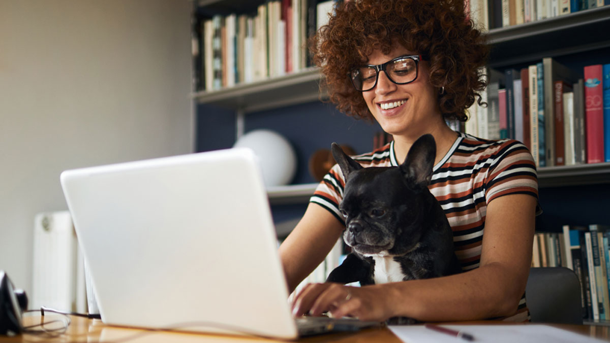 Smiling woman seated and typing on a laptop with a small dog