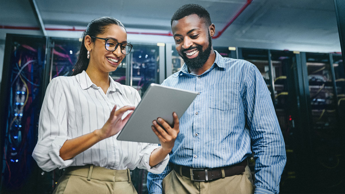 Man and woman in business attire reviewing information on a tablet while inside a data center