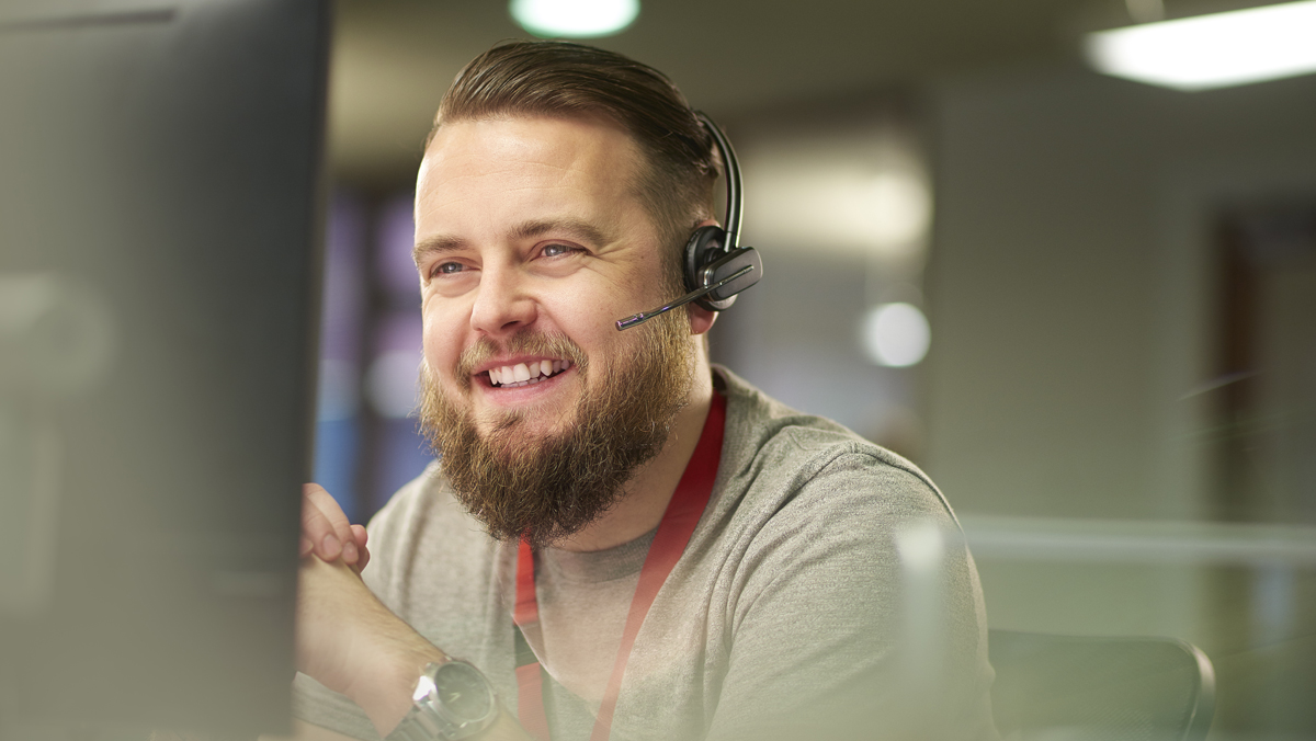 Smiling young man with a beard wearing a headset at an IT help desk